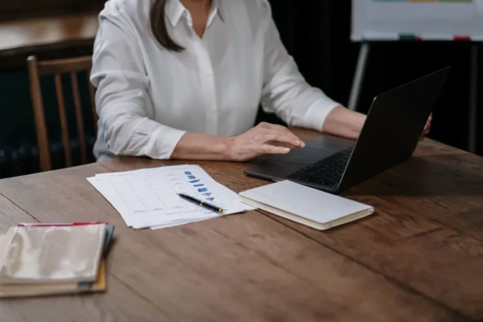 Seseorang menyusun produk digital di laptop dengan catatan ide di meja
