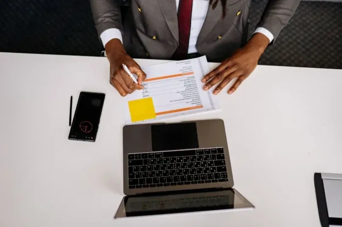 Profesional membandingkan laporan di laptop dengan dokumen bidang kerjanya